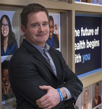 Photo of Dave Chesla smiling in front of a sign that reads "The future of health begins with you"
